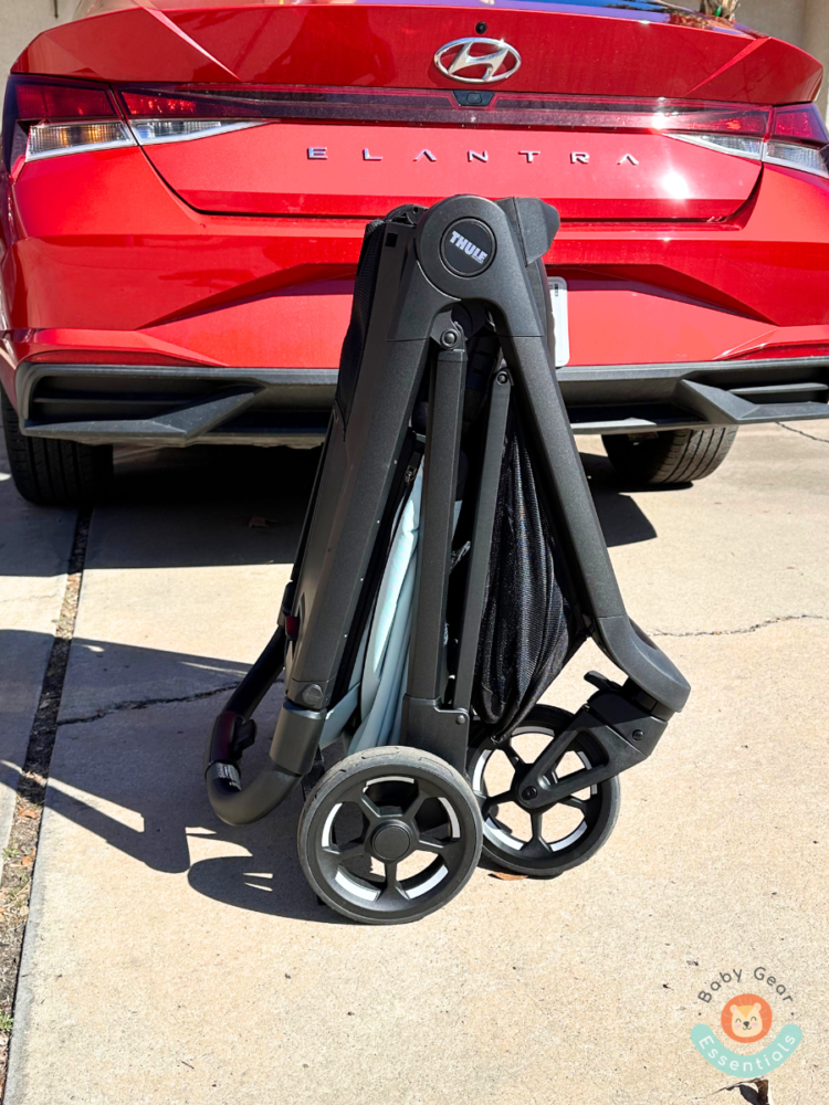 Thule Shine Stroller folded and self-standing in front of car